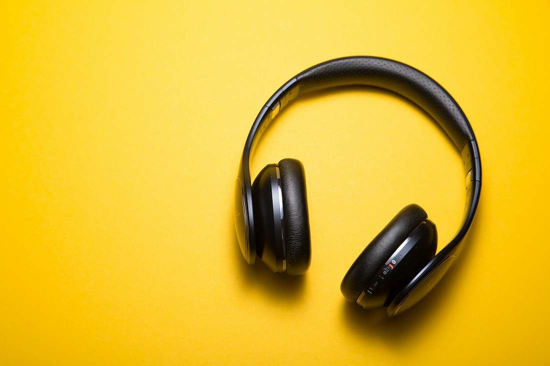Black wireless headphones against a bright yellow background